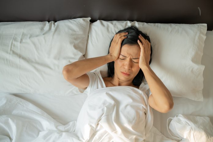 Unhappy exhausted mature woman with closed eyes lying in bed, to