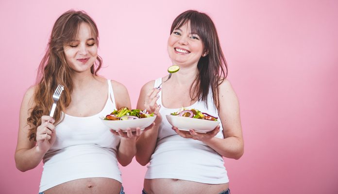 maternity concept, two pregnant woman eating fresh salad
